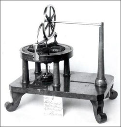Figure 9 : Moteur de Davenport, formé par deux bobines croisées, qui tournent suivant un axe vertical dans un anneau en bois muni de deux aimants permanents en forme de demi-cercle. Les bobines sont alimentées par un commutateur, visible à l'extrémité inférieure de l'axe (© Smithsonian Museum).